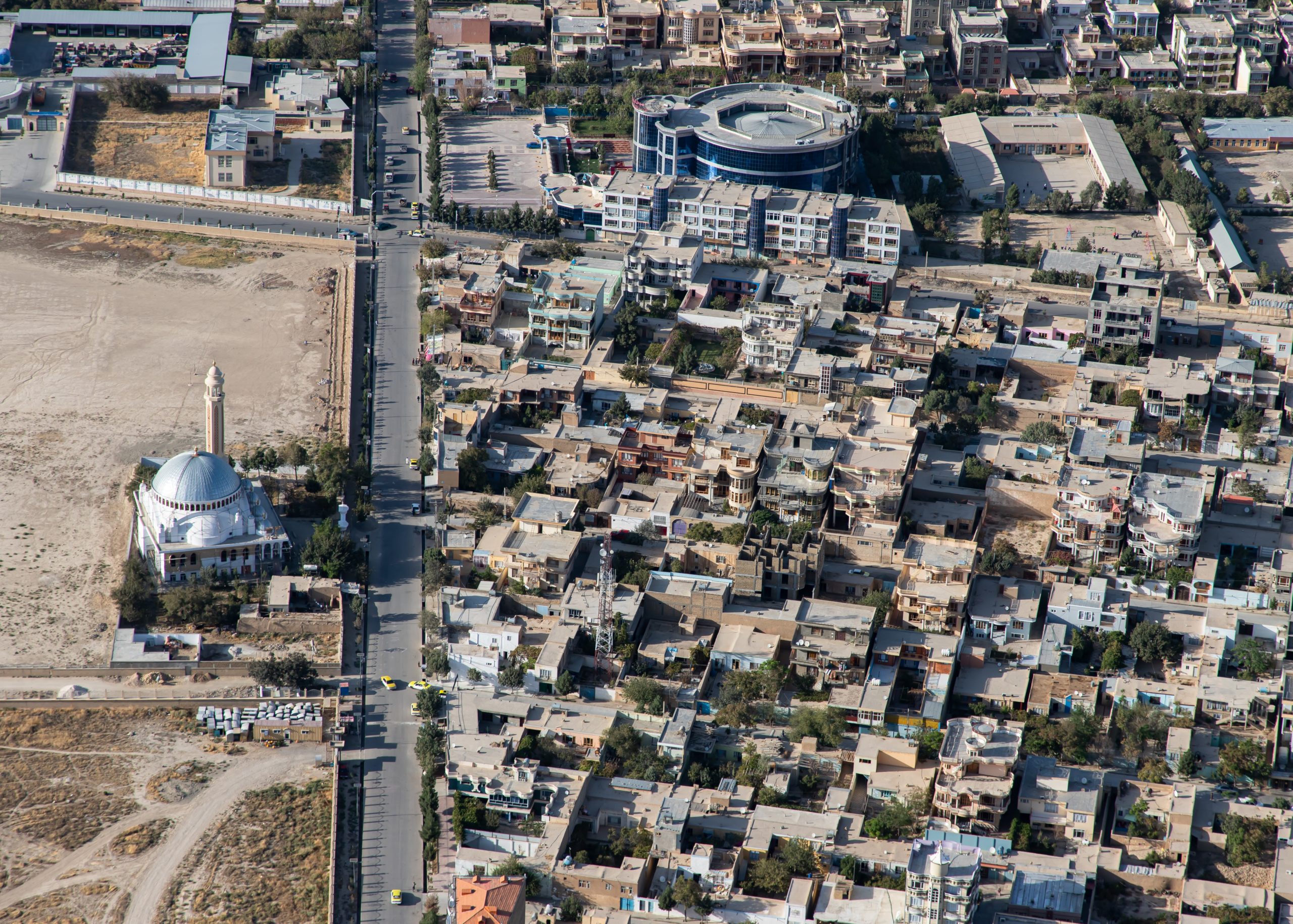 A birds-eye view of Mazar-e-Sharif in Afghanistan showing a mosque on the bottom left across the street from a city subdivision.
